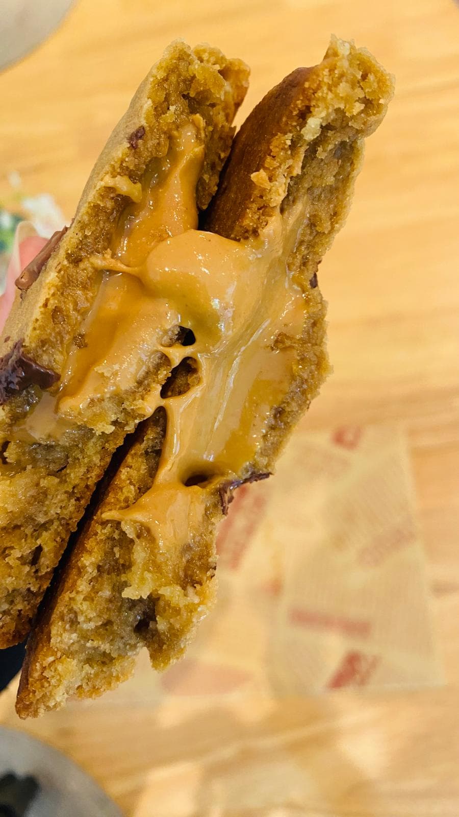 Peanut butter cookie torn open with molten peanut butter centre stretching — alternate view
